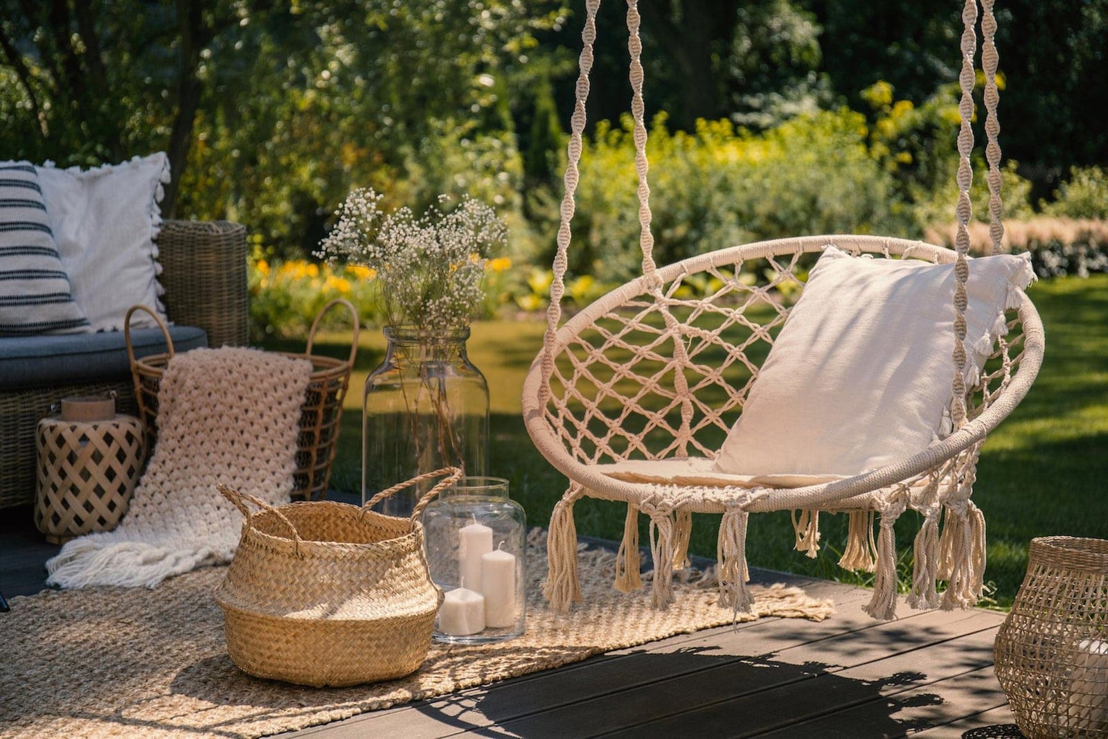 Macramé swing with a cushion, natural-fibre baskets and candles in a garden at dusk